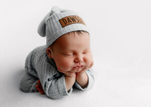 Newborn baby in froggy pose wearing baby blue and a cap
