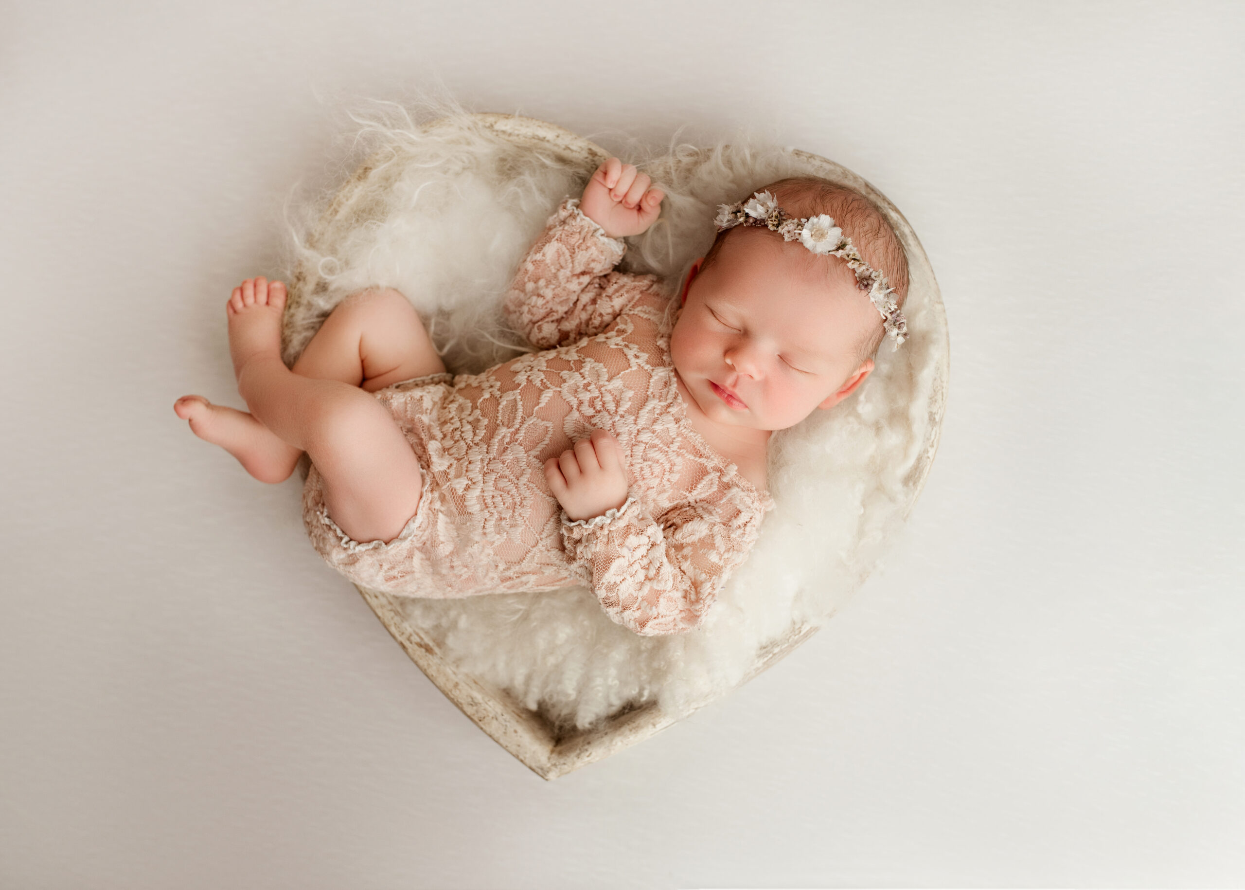 newborn laying in a heart bowl prop with fur and florals