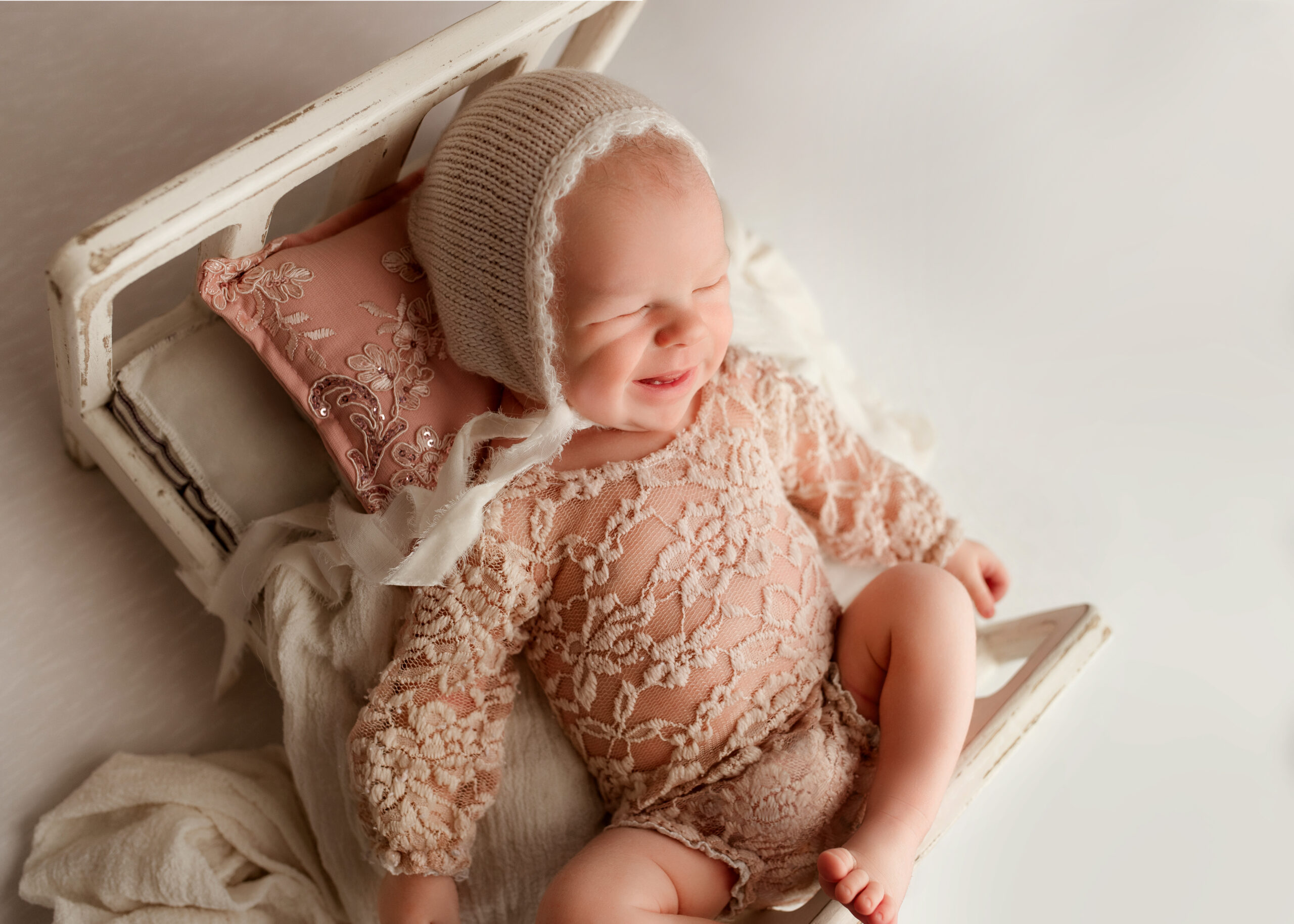 Newborn baby girl smiles in bed pose in photography studio